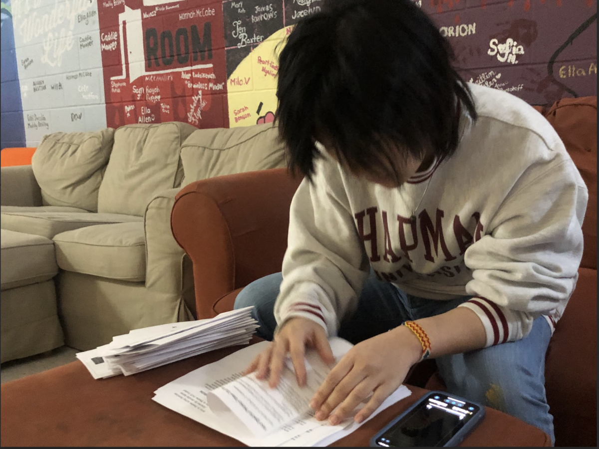 F-Wing Student Intern Chris Oh (Class of 2025) folding programs during third block for the upcoming Intro to Theatre and Acting 2 Showcase.